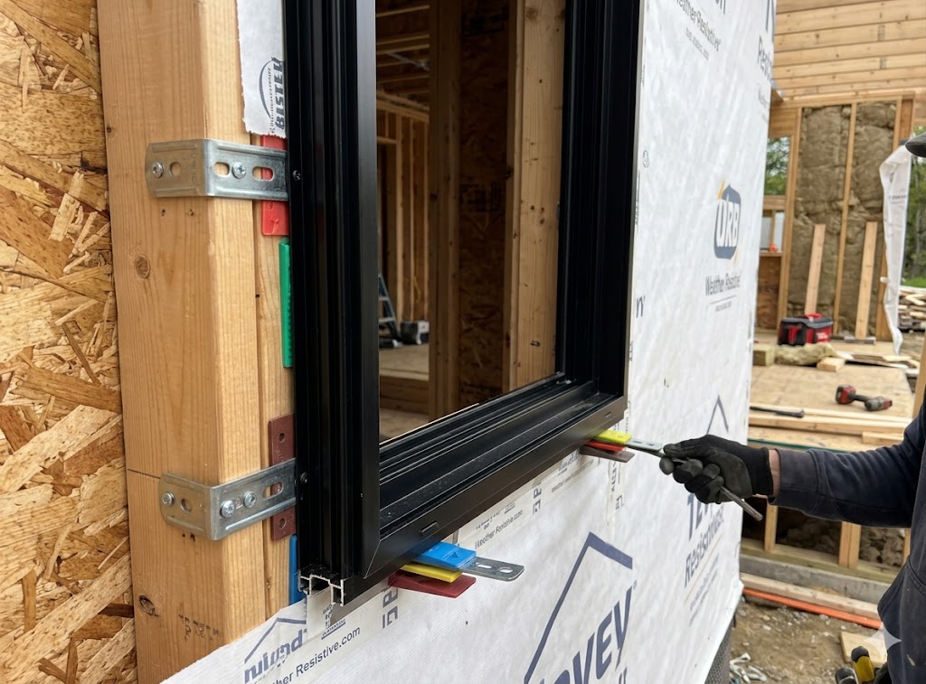 Exploded diagram showing bracket-mounted aluminum window frame, mounting brackets, shims, sill pan, and WRB flashing layers in a wood-frame wall section
