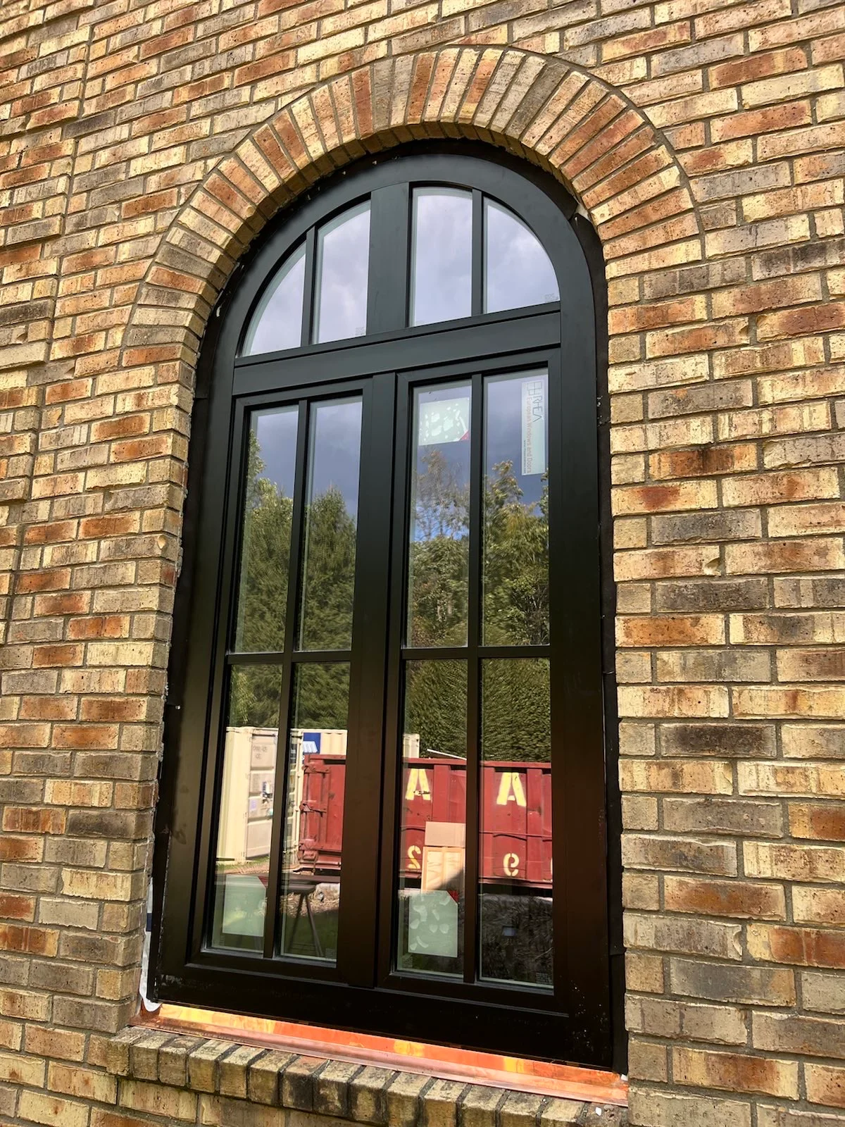 Dark arched timber window set in a brick facade